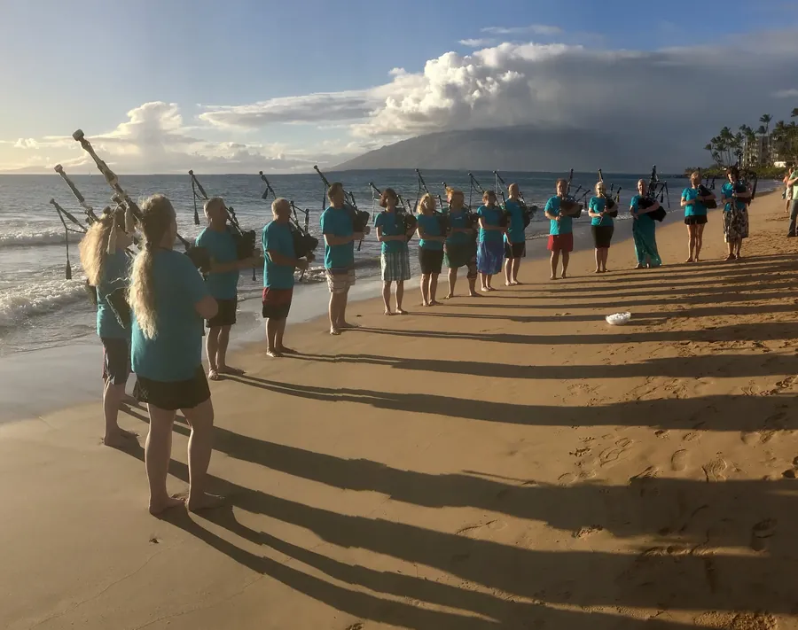 A long line of pipers on the beach at golden hour casting long shadows