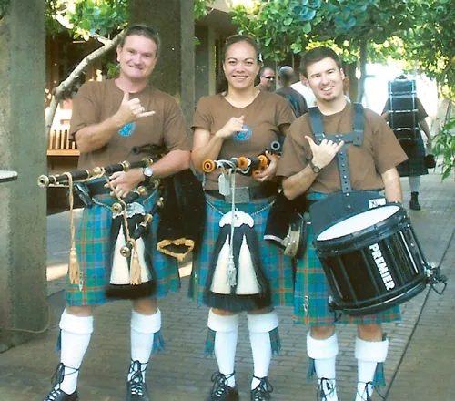 Three band members in kilts smiling with a snare drum