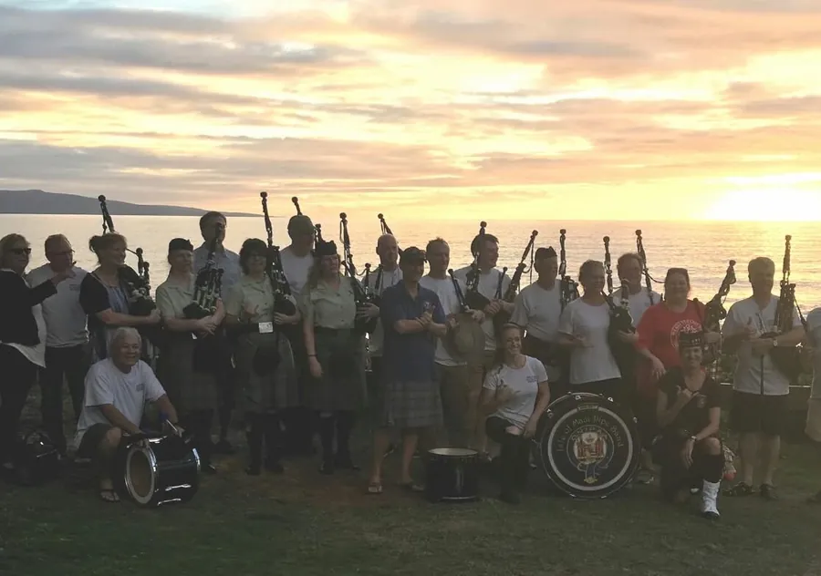 A large group of pipers by the sea at sunset