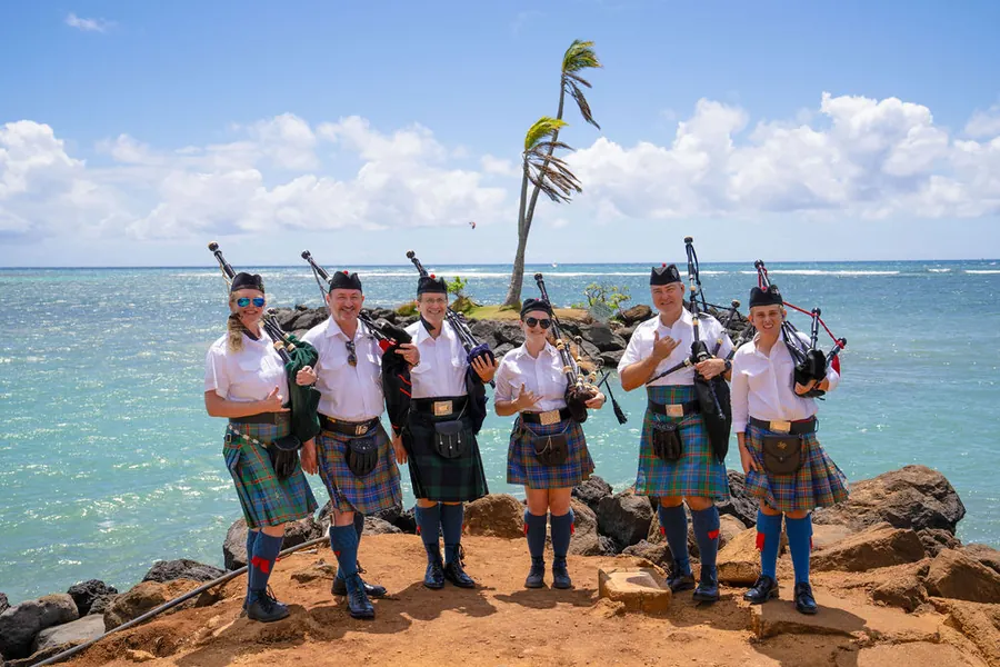 Pipers in kilts standing on a rocky point above turquoise water