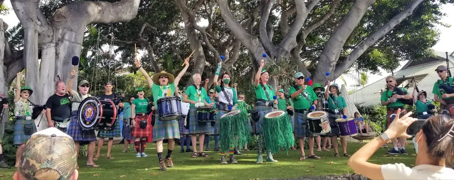 Pipers and drummers in green under a wide banyan tree
