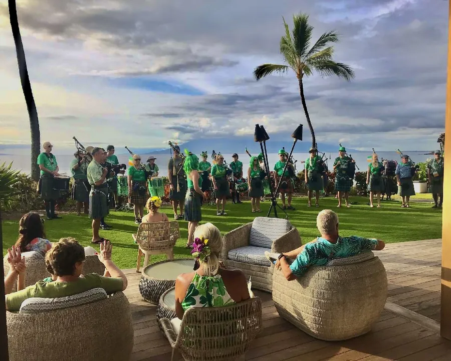 Pipers in green performing on a lawn above the ocean while guests watch
