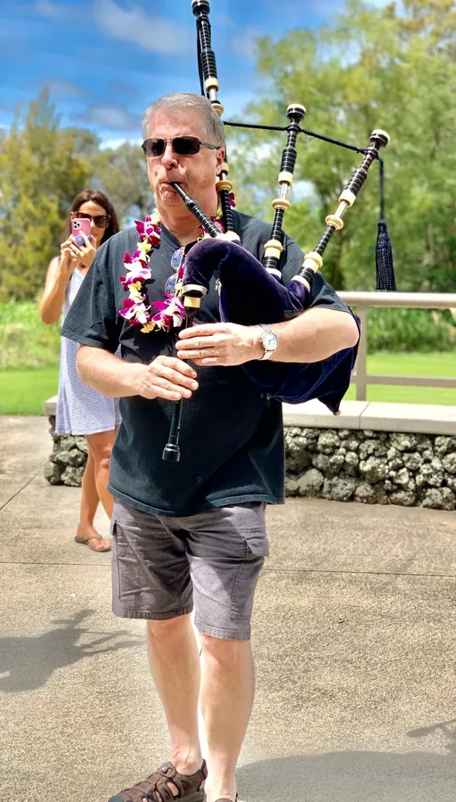 A piper in a lei and sunglasses playing outdoors