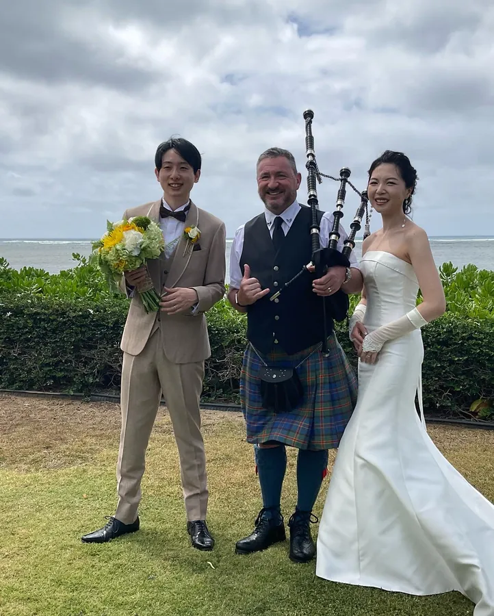 A piper in a kilt between a bride and groom