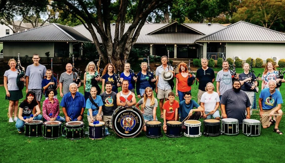 A large group of band members and family seated and standing behind a row of drums