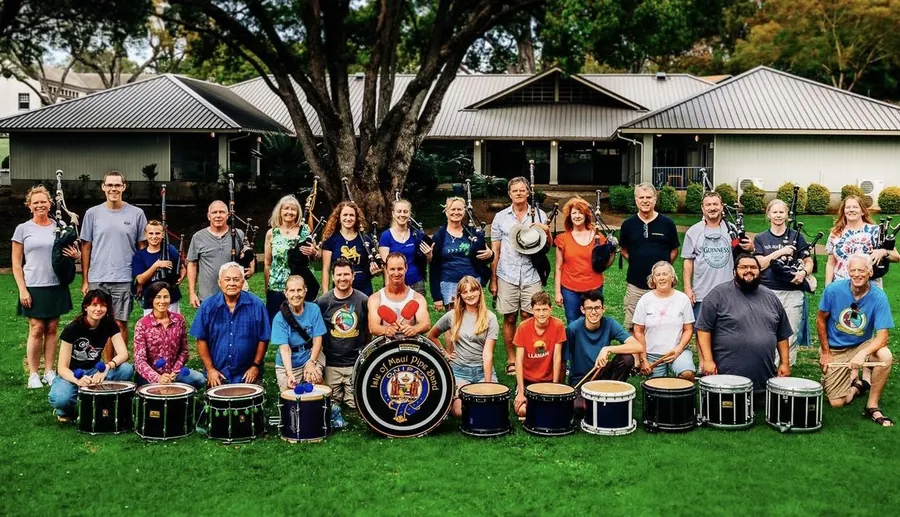A large group of band members and family seated and standing behind a row of drums