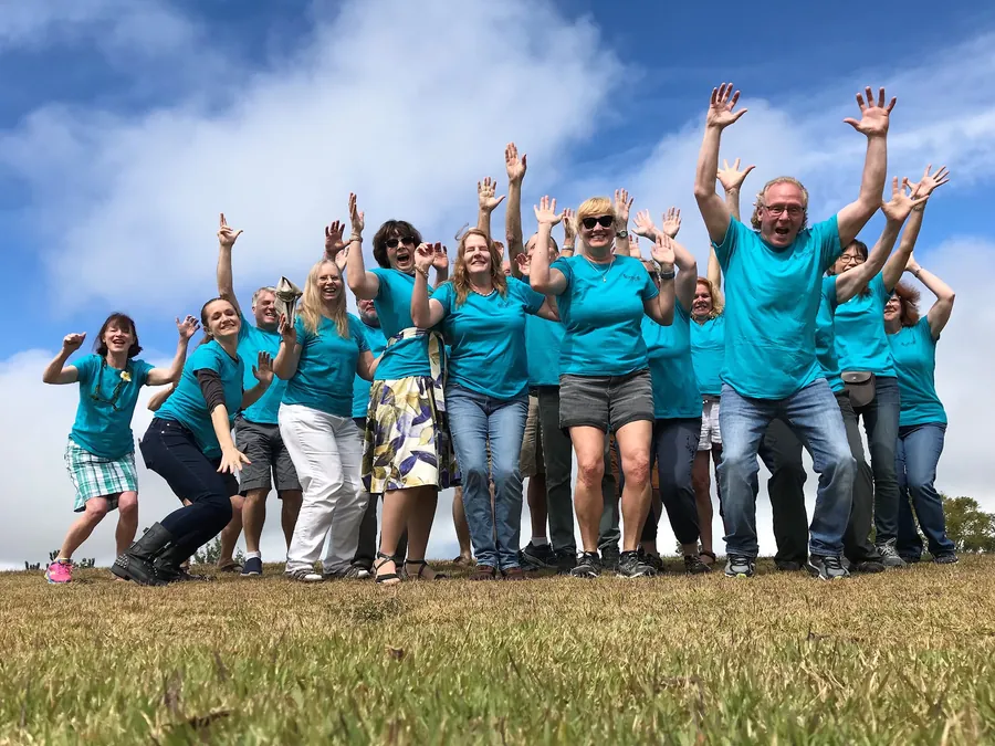 Pipe school students in matching teal shirts jumping with arms raised on a grassy hill