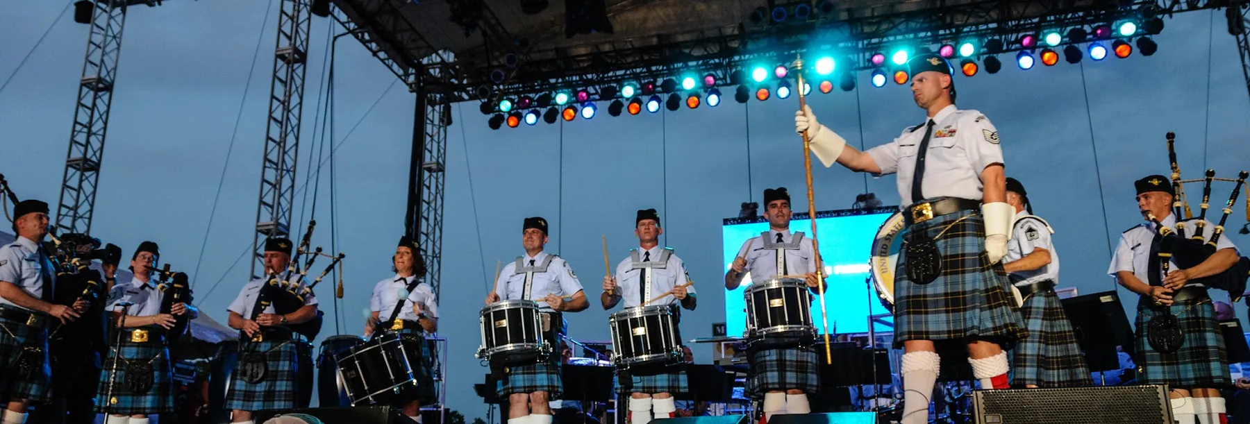 Pipers and drummers performing on a big concert stage under lights