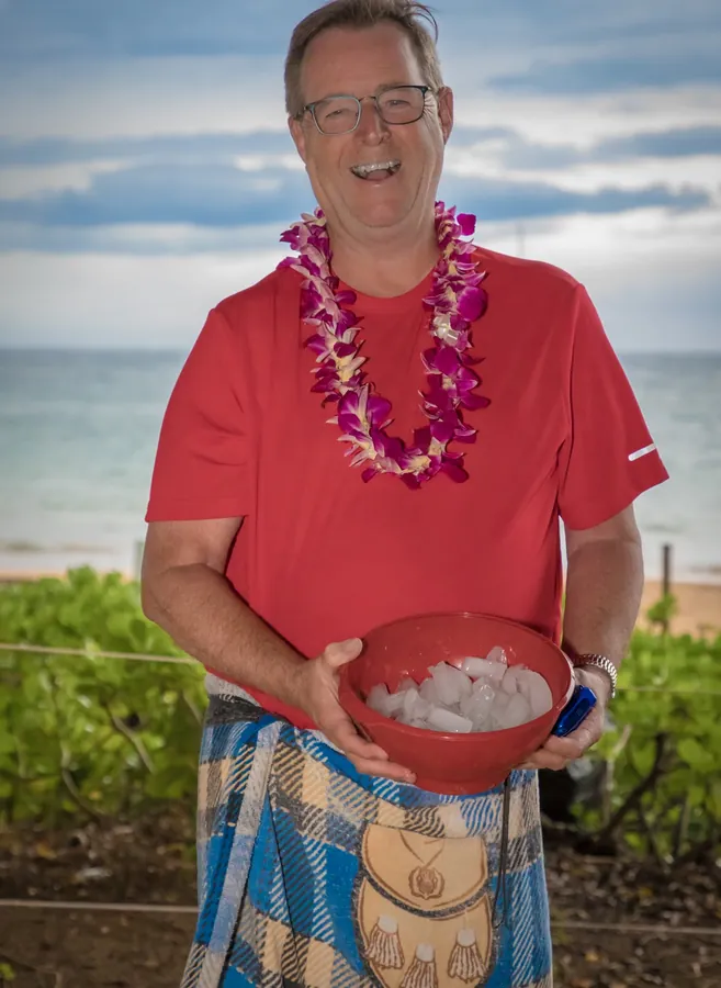 A smiling man in a lei and kilt holding a bowl