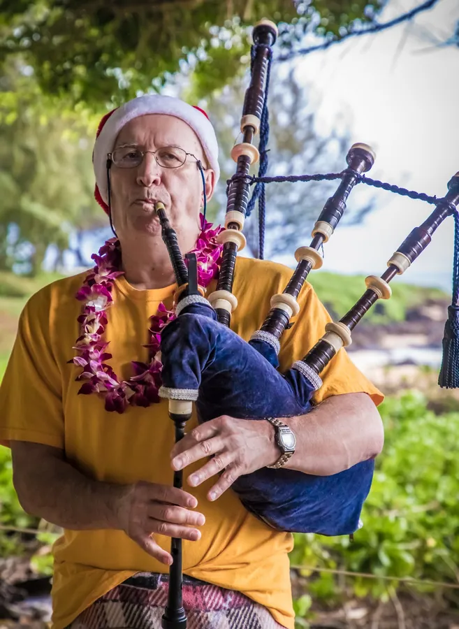 A piper in a lei and yellow shirt playing