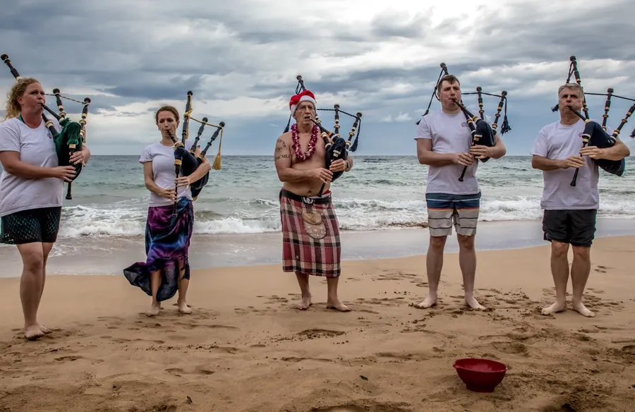 Pipers in sarongs and board shorts playing at the water