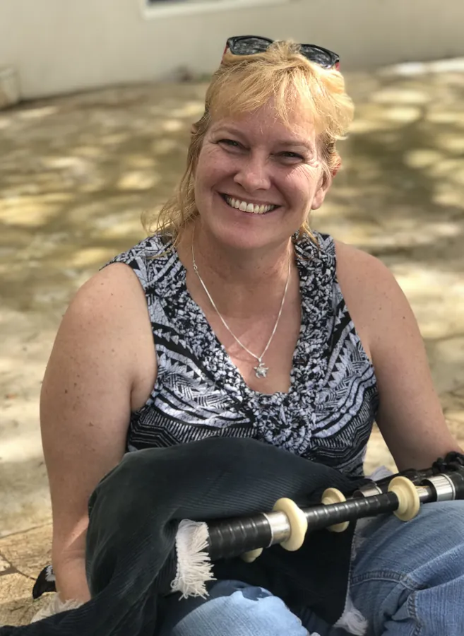 A smiling piper with her pipes on her lap
