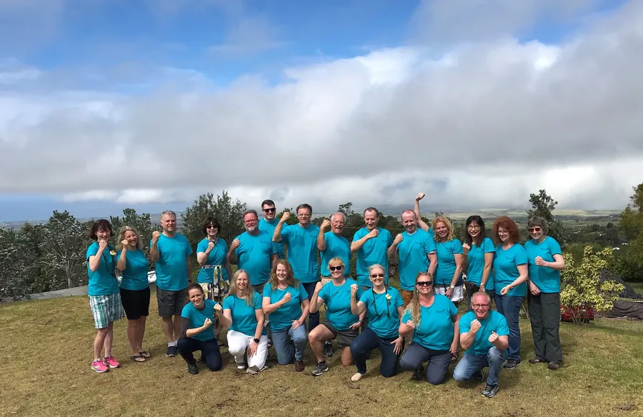 Students in teal shirts posing on a green hill